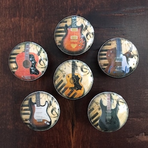 May include: Six round glass magnets with different guitar designs. Each magnet features a different guitar with a vintage look and a background of musical notes and piano keys.