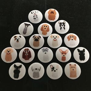 May include: A collection of 16 round, white buttons with different dog breeds illustrated on them. The buttons are arranged in a triangular shape.