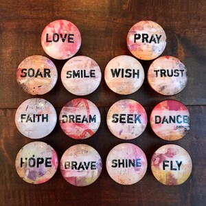 May include: A set of 14 round, colorful, decorative magnets with inspirational words printed in black. The words include: LOVE, PRAY, SOAR, SMILE, WISH, TRUST, FAITH, DREAM, SEEK, DANCE, HOPE, BRAVE, SHINE, and FLY.
