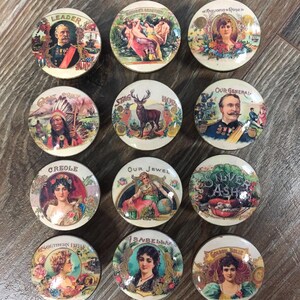 May include: Twelve round, colorful, vintage-style cigar box lids with various images, including a stag, a Native American, a woman, and a man in a military uniform. The lids are all in a circular shape and have a white background with gold trim.