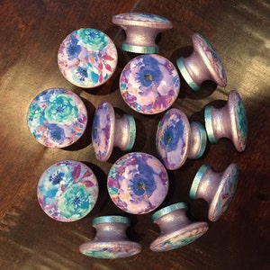 May include: A collection of 12 purple and teal floral patterned cabinet knobs with a silver metallic finish.