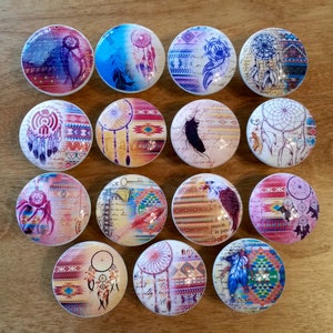 May include: Set of 15 round ceramic drawer knobs with a Native American theme. Each knob features a different design with dreamcatchers, feathers, and geometric patterns in shades of pink, blue, yellow, and brown.