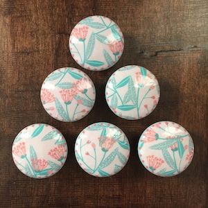 May include: Six round, white ceramic knobs with a teal blue border and a pink floral pattern. The knobs have a dotted pattern around the edge.