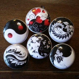 Puede incluir: Seis botones redondos de cerámica blanca con diseños yin yang en blanco y negro. Cada botón presenta un diseño diferente, incluyendo corazones, hojas y espirales.