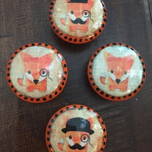 May include: Four round orange and black coasters with a cartoon fox wearing a monocle and a top hat. The fox is on a white background with a brown texture.