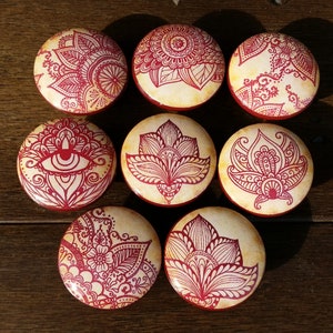 May include: Eight round wooden knobs with red and white mandala designs. The knobs have a distressed, vintage look.