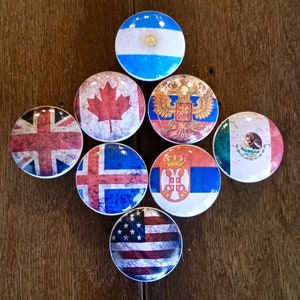 May include: Nine round, white ceramic knobs with different country flags printed on them. The flags include Canada, Argentina, Russia, Mexico, Iceland, Serbia, the United Kingdom, and the United States.