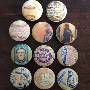 May include: Ten round, vintage-style baseball themed cabinet knobs. The knobs feature images of baseballs, players, and baseball equipment. The knobs are in various colors, including red, white, blue, and brown.