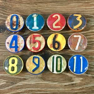 May include: Twelve round ceramic knobs with numbers 0 through 11 painted on them. The numbers are in various colors and styles, and the knobs have a distressed, vintage look.