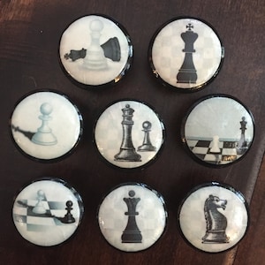 May include: A collection of eight round cabinet knobs featuring chess piece designs. Each knob has a white background with a black and white chess piece illustration, framed by a black border. The chess pieces include a king, queen, pawn, and knight.