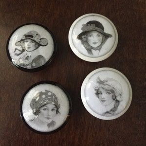 May include: Four round black and white ceramic knobs with images of women wearing hats. The women are drawn in black and white.