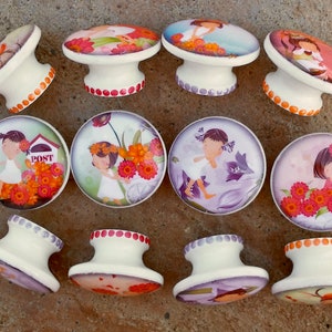 Puede incluir: Conjunto de 10 pomos de cajón de cerámica con ilustraciones coloridas de niñas y flores. Cada pomo presenta un diseño diferente con una base blanca y una parte superior colorida.