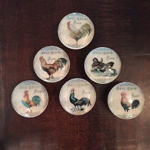 May include: Six round ceramic knobs with a white background and blue and white checkered border. Each knob features a vintage-style postcard image of a rooster or hen with the text "Post Card Farm".