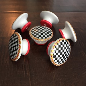 May include: Six white ceramic cabinet knobs with a black and white checkered pattern, gold trim, and red accents.