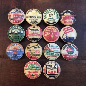 May include: A collection of 12 vintage milk bottle caps with various dairy company logos and slogans. The caps are round and feature colorful designs with red, yellow, blue, and green accents. Some of the logos include "Frates Dairy Co", "Rosebud Creamery", "Lassig's Dairy, Inc", and "Austin's Dairy".