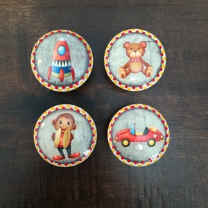 May include: Four round, colorful, decorative knobs with different designs. The knobs feature a rocket ship, a teddy bear, a monkey playing a drum, and a red race car.
