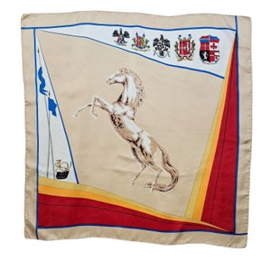 May include: A beige silk scarf with a red, yellow, and blue border. The center of the scarf features a white horse rearing up on its hind legs. The scarf also has a series of crests and shields in the top left corner.