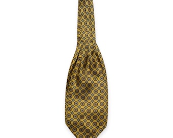 May include: A yellow ascot tie with a repeating circular pattern in brown and olive green. The tie is folded and draped, showcasing the intricate design. This formal neckwear adds a touch of elegance.