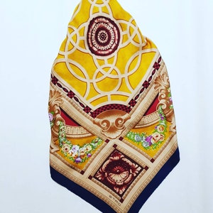 May include: A yellow, red and blue silk scarf with a geometric pattern and floral accents. The scarf features a central design of interlocking circles and a smaller floral design in the bottom corner. The brand name "ETRO" is printed in the bottom corner.
