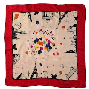 May include: A white silk scarf with a red polka dot border. The scarf features a black and white illustration of famous landmarks, including the Eiffel Tower, the Statue of Liberty, and the London Eye. The text "I ♥ Codella" is printed in black on the scarf.
