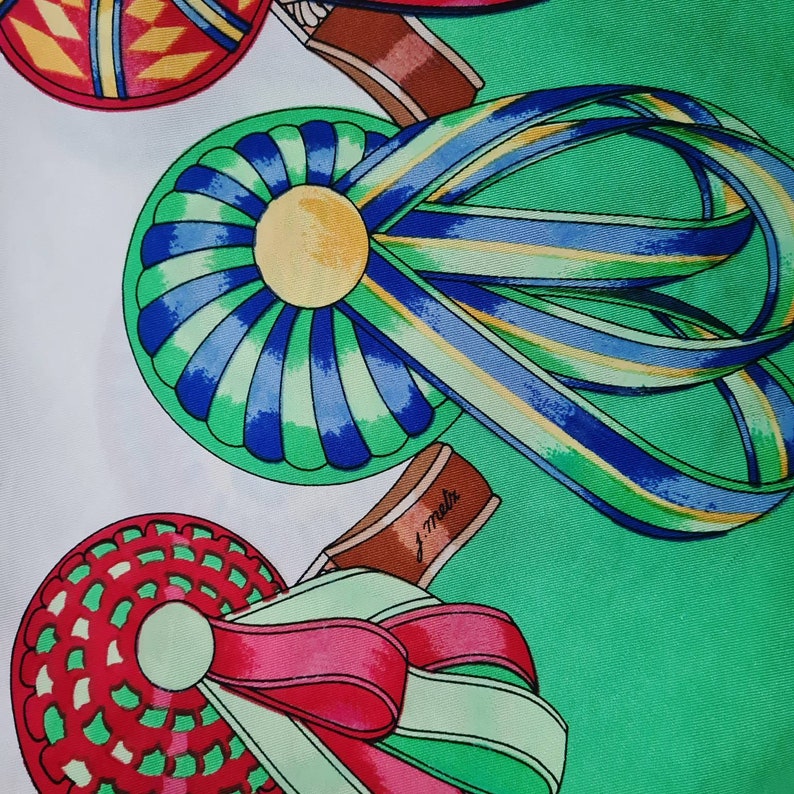 May include: A green, blue, and yellow ribbon tied around a green and blue circular design with a yellow center. The ribbon is tied around a brown object with the text "J. Melk" on it. The background is green.