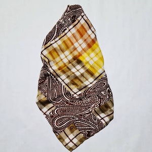 Peut inclure: Une &eacute;charpe &agrave; motif paisley brun et jaune avec un motif &agrave; carreaux. L'&eacute;charpe est pli&eacute;e en deux et a une bordure frang&eacute;e.