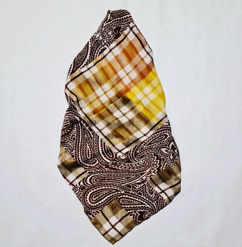 Peut inclure: Une &eacute;charpe &agrave; motif paisley brun et jaune avec un motif &agrave; carreaux. L'&eacute;charpe est pli&eacute;e en deux et a une bordure frang&eacute;e.