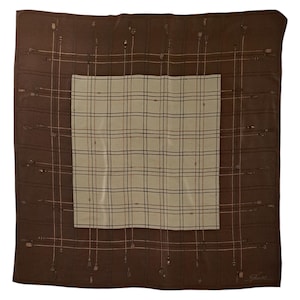 May include: A square brown scarf with a cream-colored plaid center. The brown border features a repeating pattern of thin lines and small, decorative elements. The scarf is likely made of silk or a similar fabric.
