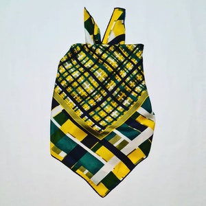 May include: A yellow, green, and black patterned silk scarf with a geometric design. The scarf has a triangular shape and is folded into a knot at the top.