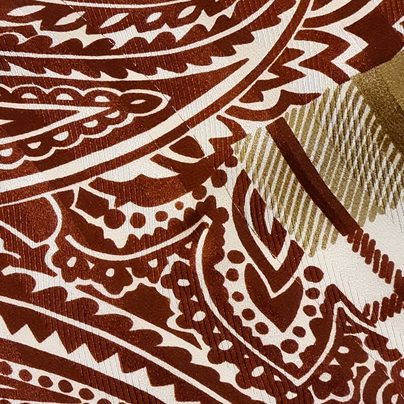 Peut inclure: Gros plan sur un tissu &agrave; motif paisley brun et blanc avec un motif ray&eacute; or et blanc dans le coin sup&eacute;rieur droit.
