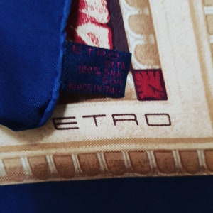 May include: A blue silk scarf with a beige and red pattern. The scarf has a label that reads "ETRO 100% SETA SILK SOIE MADE IN ITALY".