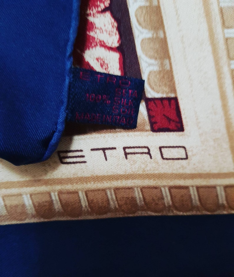 May include: A blue silk scarf with a beige and red pattern. The scarf has a label that reads "ETRO 100% SETA SILK SOIE MADE IN ITALY".