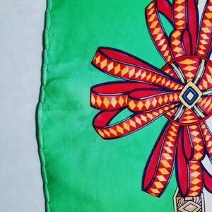 May include: A green silk scarf with a large red and yellow bow. The bow has a diamond pattern and is tied in a knot.