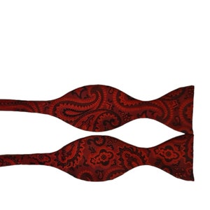 May include: A red bow tie with a paisley pattern. The bow tie is made of a silky fabric.
