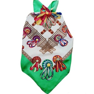 May include: A green and white silk scarf with a pattern of colorful ribbons and rosettes. The scarf has a triangular shape and a fringed edge.