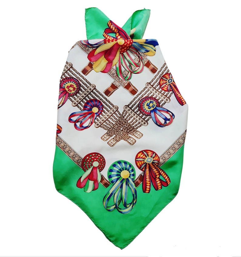 May include: A green and white silk scarf with a pattern of colorful ribbons and rosettes. The scarf has a triangular shape and a fringed edge.