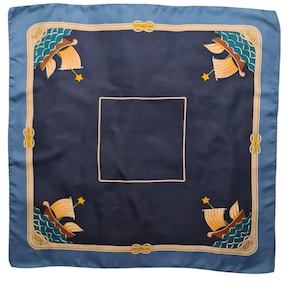 Könnte beinhalten: Quadratisches marineblaues Tuch mit hellblauem Rand. Das Tuch hat ein nautisches Design mit Segelbooten, Wellen und Sternen in den Ecken. Ein cremefarbener, seilartiger Rand umrahmt das Design.