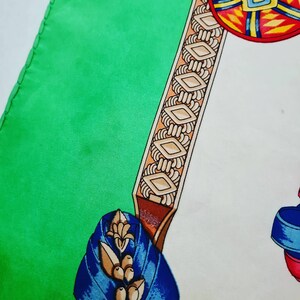 May include: A green and white silk scarf with a colorful geometric design. The scarf features a brown and gold border with a repeating diamond pattern.