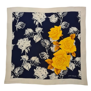 Pode incluir: Um lenço de seda branco com fundo azul marinho e um padrão floral. As flores são rosas amarelas com folhas brancas. O lenço tem o texto "pierre balmain" no canto inferior direito.