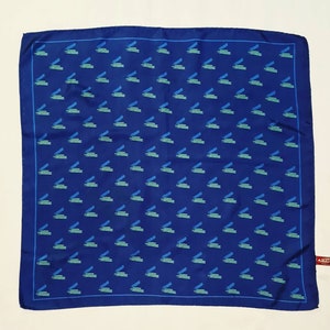 Puede incluir: Un pañuelo de seda azul con un patrón repetido de libros apilados verdes y azules.