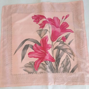 May include: A pink silk scarf with a floral design featuring pink lilies and gray leaves. The scarf has a delicate lace border.