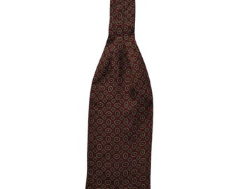 May include: A burgundy ascot tie with a repeating pattern of olive green ovals and squares. The tie is made of a smooth fabric and is designed to be worn around the neck.