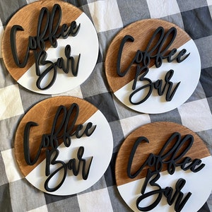 Peut inclure: Quatre pancartes rondes en bois avec un design peint en blanc et brun. Chaque pancarte porte l'inscription "Coffee Bar" en lettres 3D noires.