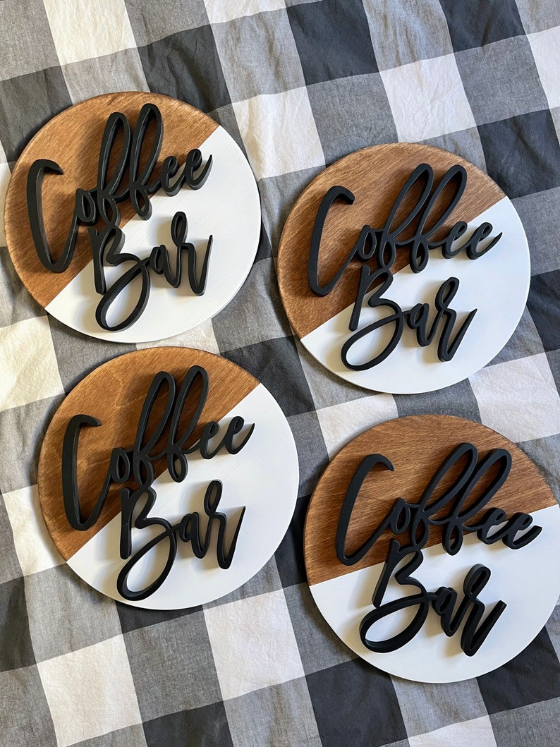 Peut inclure: Quatre pancartes rondes en bois avec un design peint en blanc et brun. Chaque pancarte porte l'inscription "Coffee Bar" en lettres 3D noires.