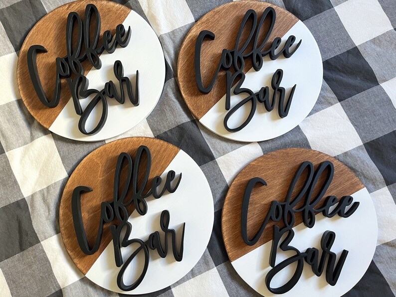 Peut inclure: Quatre pancartes rondes en bois avec un design peint en blanc et brun. Chaque pancarte porte l'inscription "Coffee Bar" en lettres 3D noires.