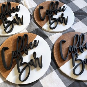 Peut inclure: Quatre pancartes rondes en bois avec un design en bois blanc et brun. Chaque pancarte porte l'inscription "Coffee Bar" en lettres 3D noires.
