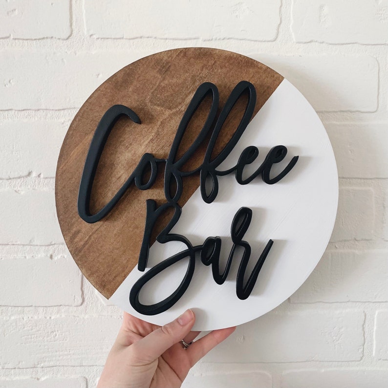 Peut inclure: Une enseigne ronde en bois avec un design divis&eacute; en blanc et brun. L'enseigne indique "Coffee Bar" en lettres d'&eacute;criture noires.
