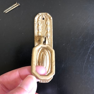 May include: Gold-toned metal drawer pulls with a decorative design. The pulls have a ring handle and are rectangular in shape.