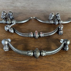 May include: Set of five antique-style cabinet hardware pulls with a dark bronze finish. The pulls have a curved shape with ornate details and a rounded knob at the end.