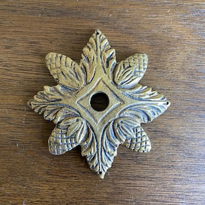 May include: A gold-toned metal decorative rosette with a detailed design of leaves and pinecones. The rosette has a central hole.